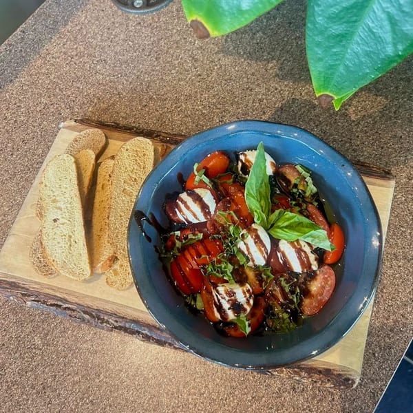Caprese salad with tomatoes, mozzarella, basil, balsamic glaze, and sliced bread on a wooden board.