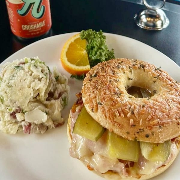 Bruchelle's Bagel Bistro's bagel sandwich with melted cheese, pickles, potato salad, and orange slice.