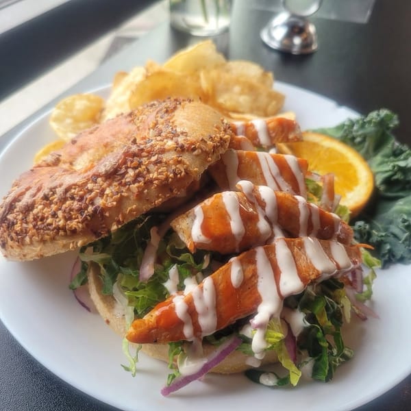 Bruchelle's Bagel Bistro's chicken bagel sandwich with chips, orange slice, and greens.