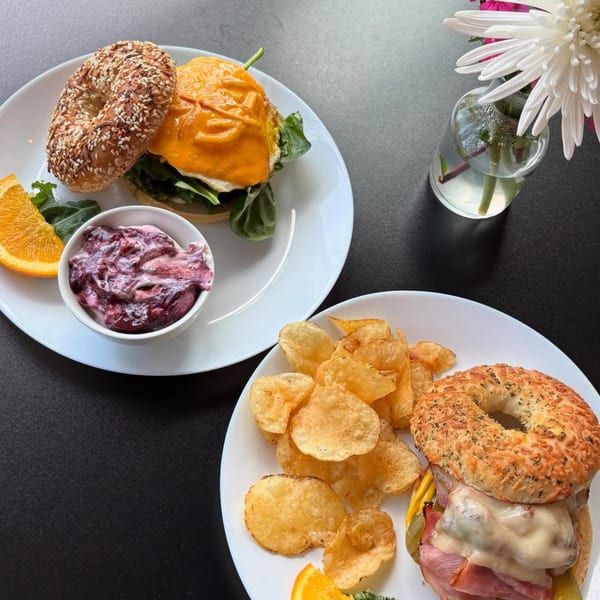 Two bagel sandwiches, one with egg and cheese, the other with ham and melted cheese, served with chips.