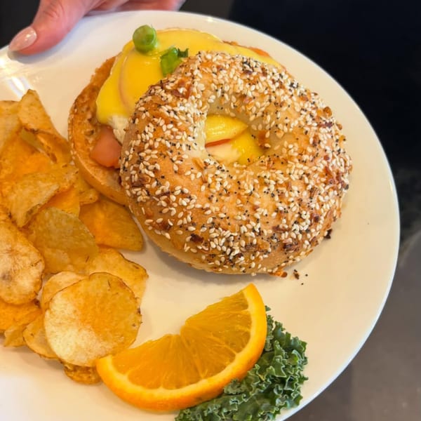 Bruchelle's Bagel Bistro's bagel with eggs benedict, chips, and an orange slice on a white plate.